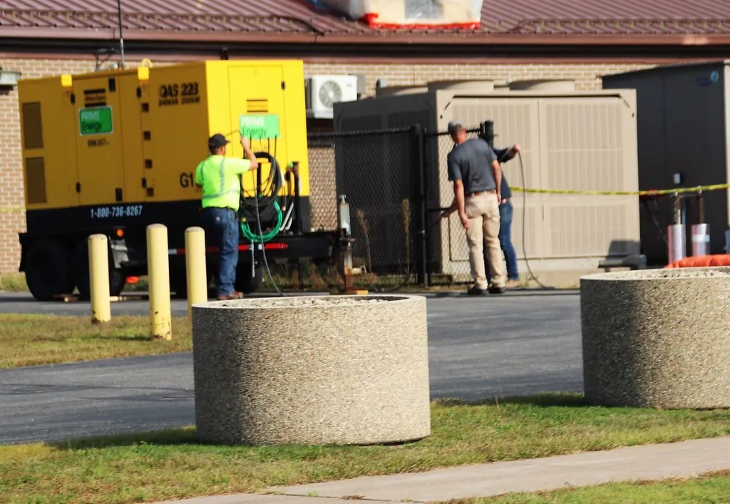Generator set di area luar gedung dengan petugas yang sedang bekerja